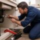 A plumber fixing a leaking pipe under a kitchen sink in a modern home.