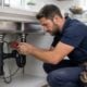 A plumber working under a kitchen sink fixing pipes and drains.